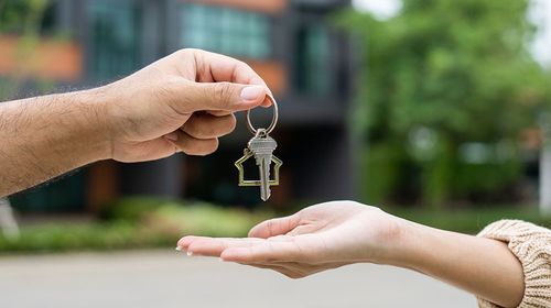 A hand holds out a house key to another open hand with palm up
